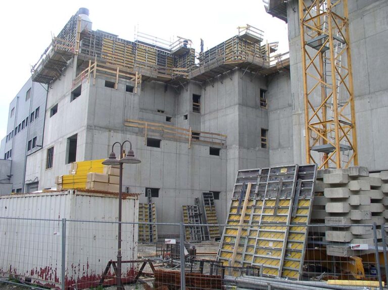 Baustelle eines modernen Mehrfamilienhauses mit sichtbarer Außenwand und Baugerüsten, umfasst Betonwände und Bauaufzüge, symbolisiert Fortschritt im Bauwesen und nachhaltiges Wohnungsbauprojekt.