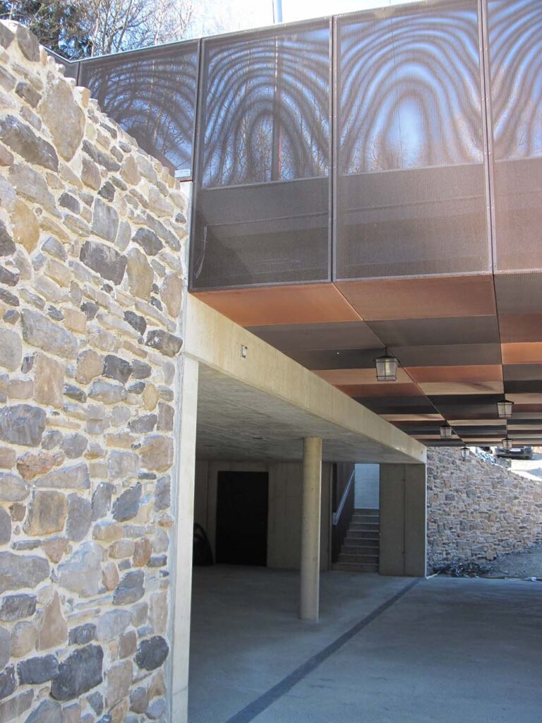 Modernes Gebäude mit Steinfassade und Balkon, nachhaltige Architektur, stilvolle Verblendmauerung, innovative Baumaterialien, zeitgemäßes Design, betonierte Flächen, Untergeschoss mit Treppenaufgang, zeitgenössisches Baukonzept, moderne Baukunst, klare Linienführung, energieeffiziente Bauweise, ländliche und urbane Elemente, wetterfeste Fassadengestaltung, hochwertige Baumaterialien, Bauprojekt in Österreich, Architektur in Graz.