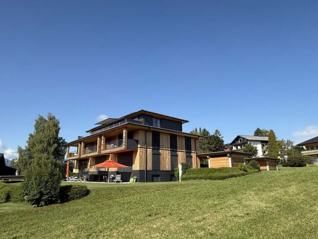 Moderne Holzarchitektur eines Ferienhauses in einer grünen Landschaft mit sonnigem Himmel.
