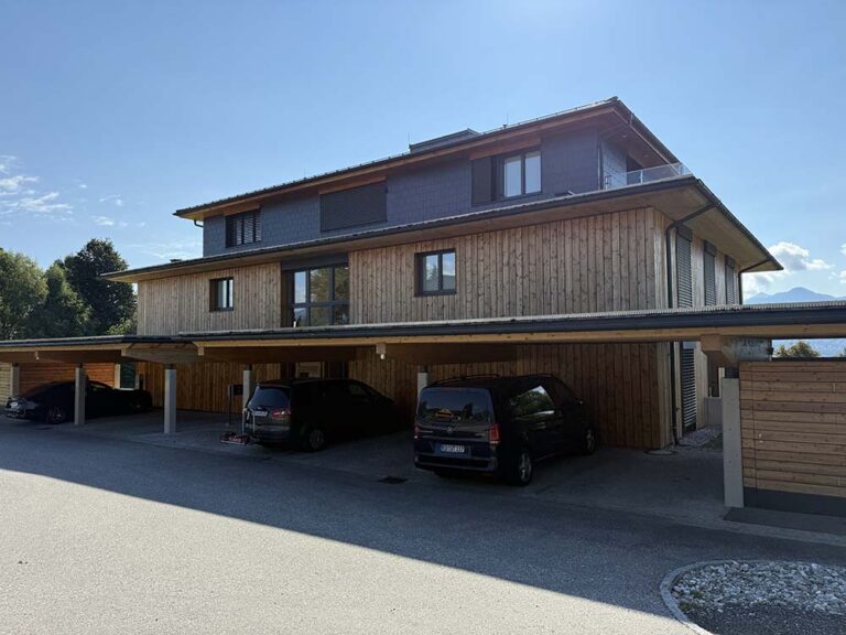 Moderne Mehrfamilienhaus mit Holzfassade und Carport, attraktive Wohnanlage in ruhiger Lage in den Bergen.