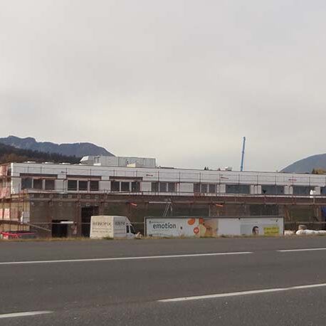 Flachdachiges Bauprojekt im Industriegebiet, im Hintergrund ist eine Berglandschaft sichtbar.