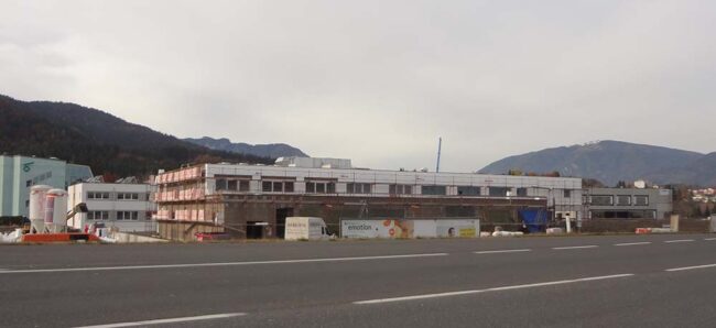 Flachdachiges Bauprojekt im Industriegebiet, im Hintergrund ist eine Berglandschaft sichtbar.