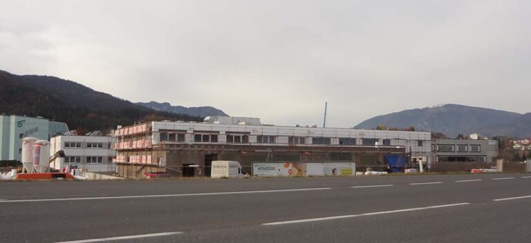 Flachdachiges Bauprojekt im Industriegebiet, im Hintergrund ist eine Berglandschaft sichtbar.