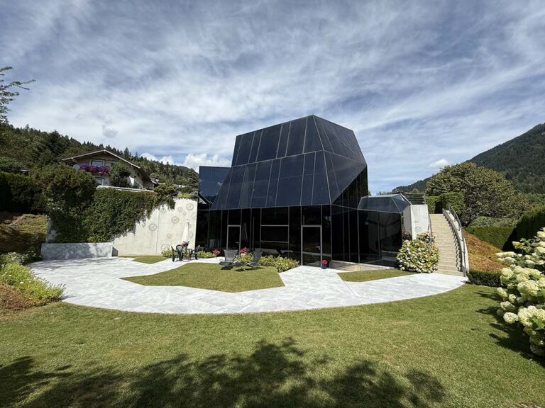 Moderne Architektur eines gläsernen Hauses in alpiner Lage mit Garten und umliegenden Bergen, perfekt für nachhaltiges Bauen und innovative Baukonzepte.