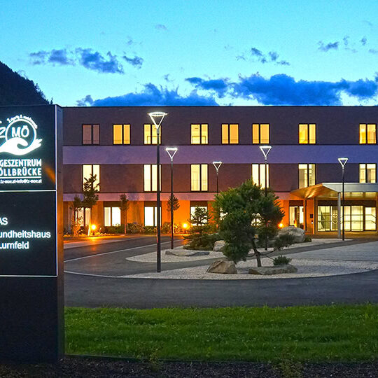 Modernes Gesundheitszentrum in den Alpen bei Nacht, blick auf das Tageszentrum Möllbrücke mit ansprechender Außenbeleuchtung und ruhiger Umgebung.