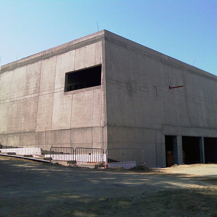 Rohbau eines modernen Gebäudes aus Beton, im Bau befindlich, kaum fertiggestellt, auf einem Baugrundstück in einer Stadt in Österreich, Baustelle mit Sicherheitsbarrieren, klarem Himmel, aktuelle Bauphase.