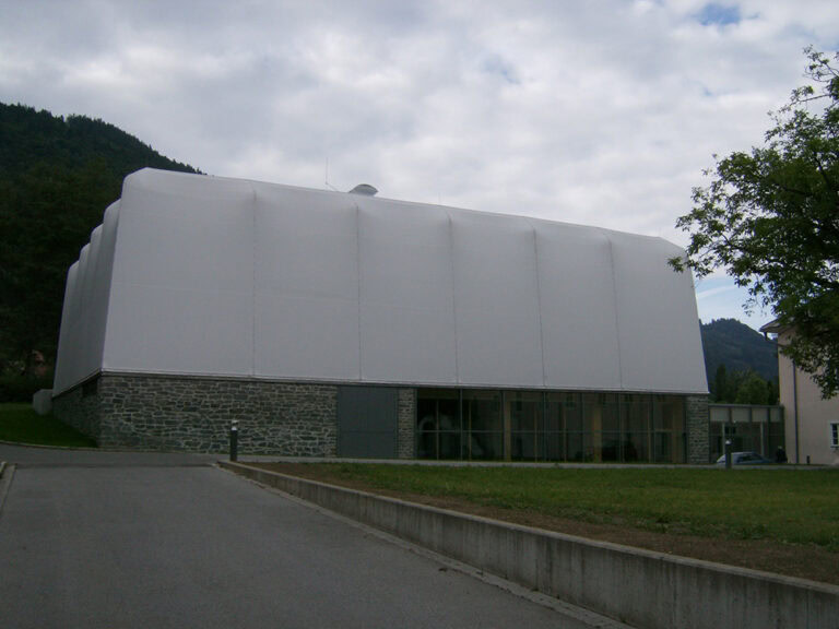 Moderne Architektur des Gebäudes mit weißer Außenhaut und Natursteinfundament in landschaftlicher Umgebung.