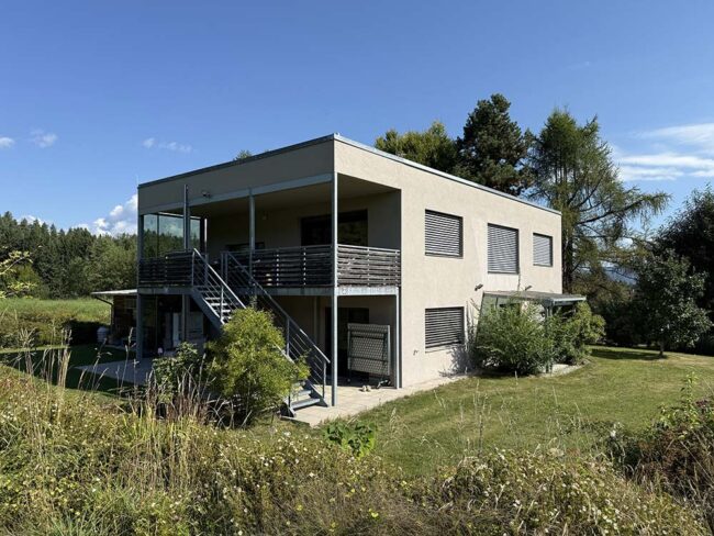 Moderne, zweistöckige Villa mit Terrasse im Grünen, umgeben von Bäumen und Wiesen, bei perfektem Wetter. Perfekt für nachhaltiges Bauen und zeitgenössisches Design.