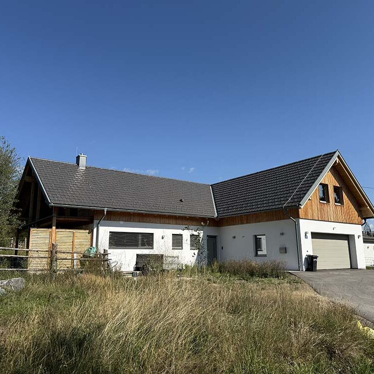 Modernes Landhaus mit Holzfassade und großen Fenstern, umgeben von Grünfläche, ideal für erholsames Wohnen im Grünen.