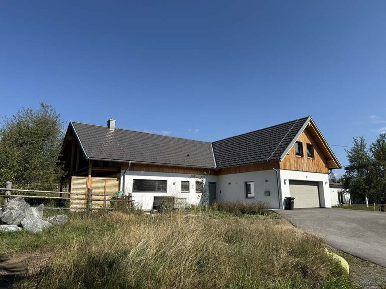 Modernes Landhaus mit Holzfassade und großen Fenstern, umgeben von Grünfläche, ideal für erholsames Wohnen im Grünen.