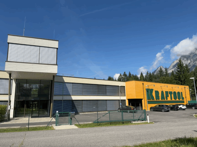 Kraftool Firmengebäude in Täler mit moderner Architektur, umgeben von Alpenlandschaft, blauer Himmel, Parkplätze vor der Firma, ideal für Werkzeuge und Bauausrüstung.