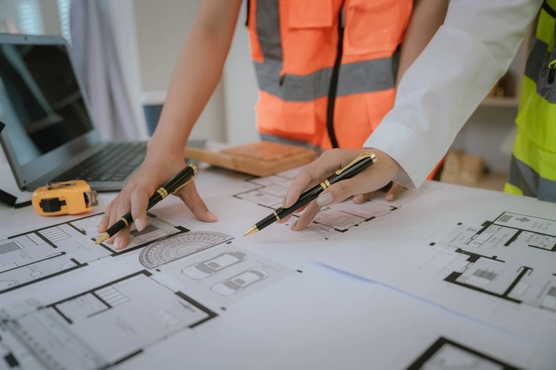 Vorplanung & Entwurf Modernes Bauplanungsgespräch mit Architekten auf Bauplänen, Bauzeichner bei der Arbeit, Handzeichnungen und technische Skizzen für Bauprojekte.